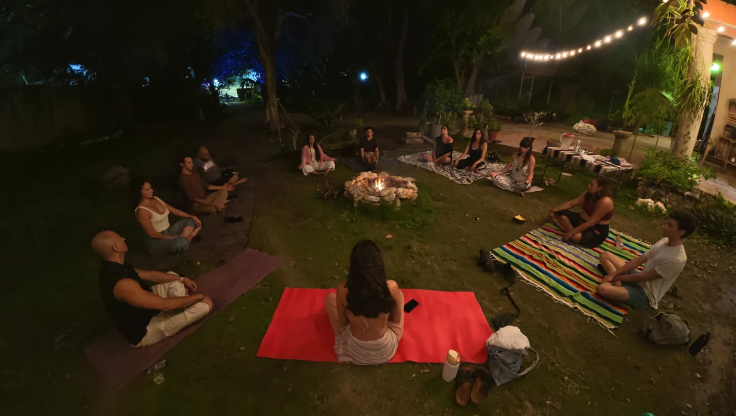 Grupo sobre colchonetas al aire libre de noche, bajo guirnaldas de luces.