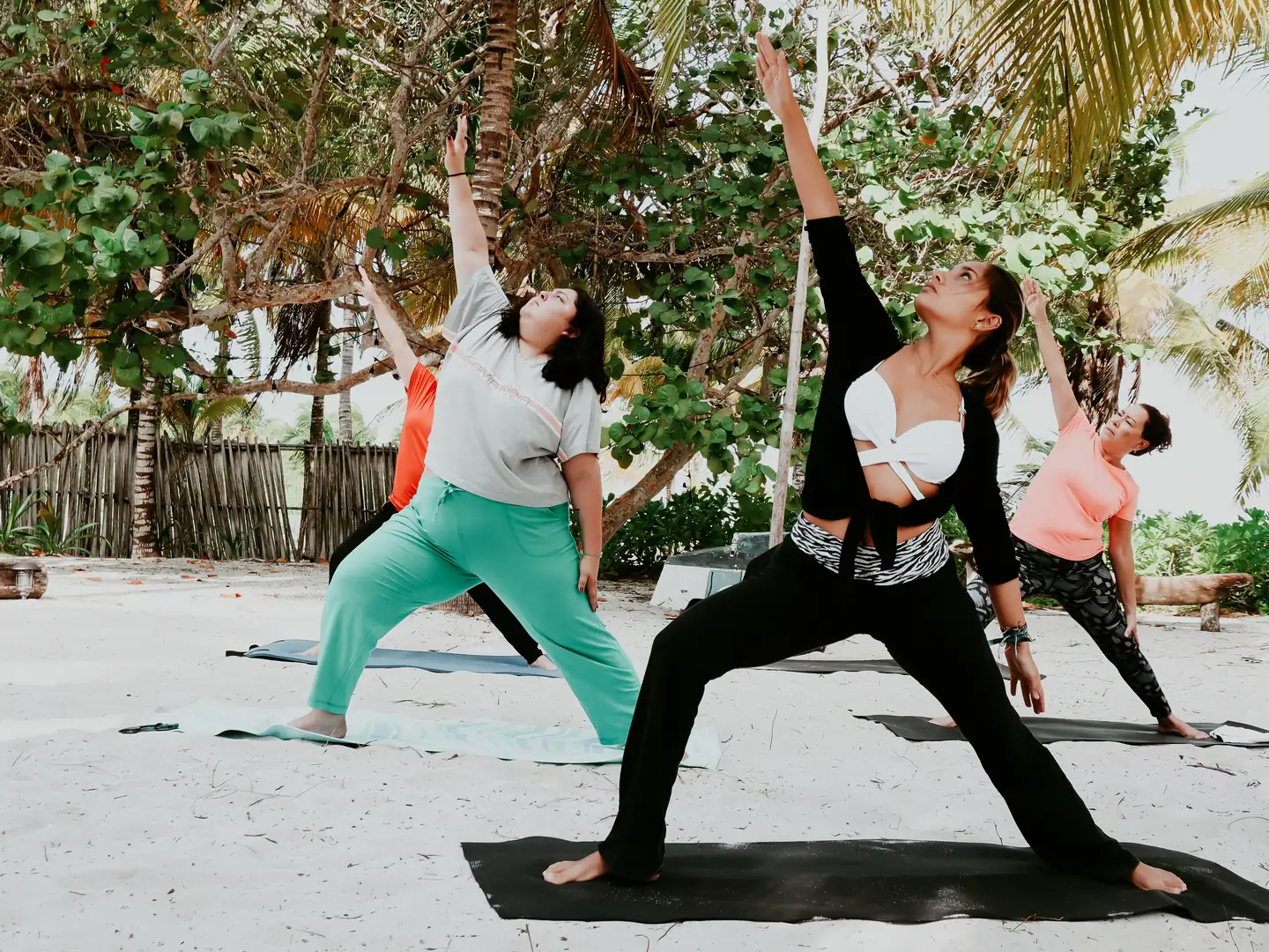 Grupo practicando yoga sobre colchonetas en la arena, rodeado de vegetación tropical.