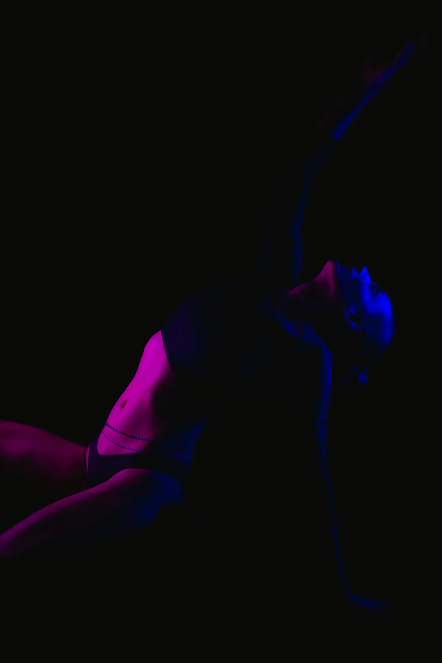 Figura danzando en la oscuridad con luces azules, violetas y magenta.